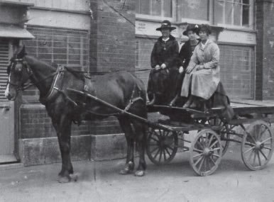 Black and white picture of three women sat on a horse cart
