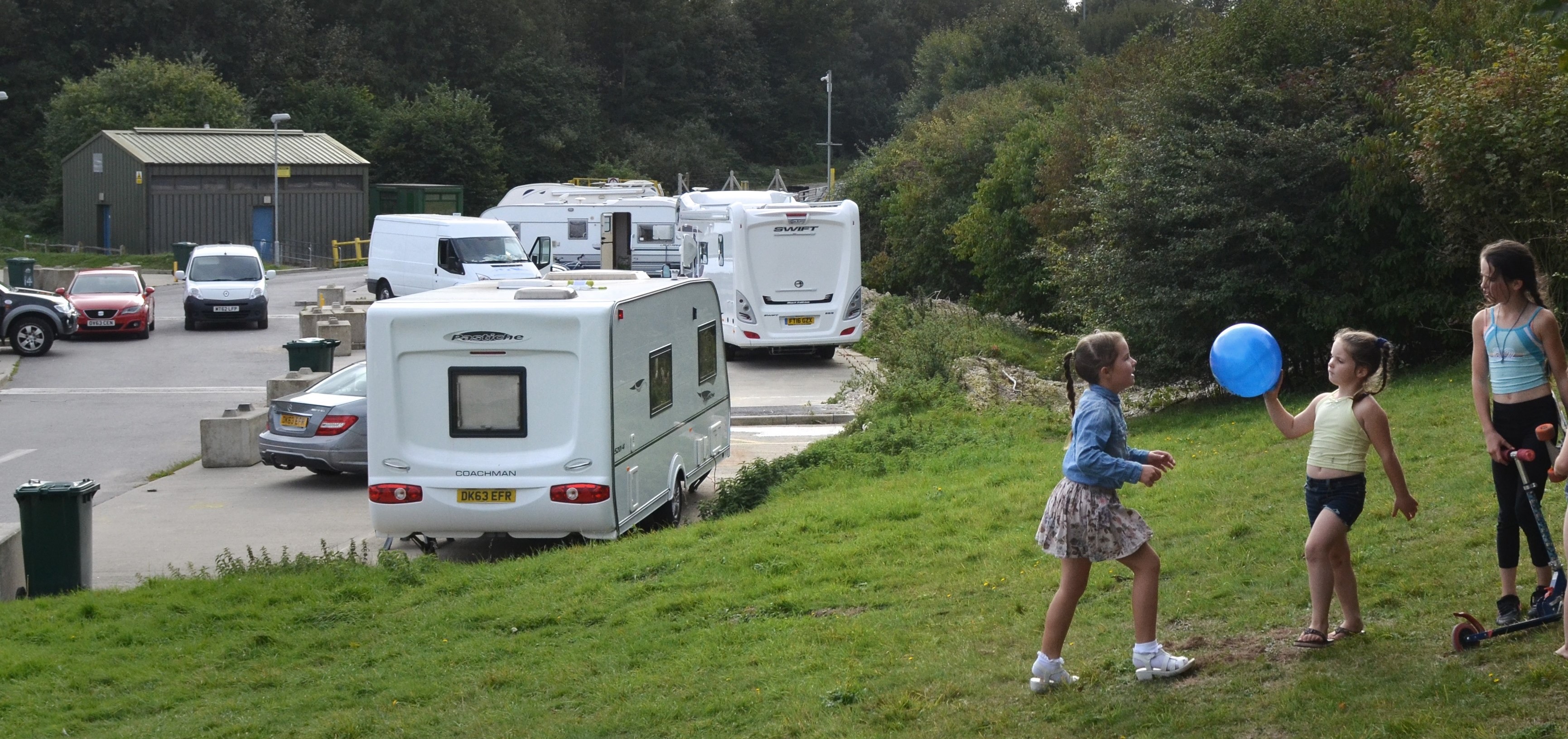 Girls playing on grass verge, next to trailers on a site