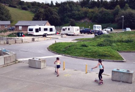 Picture of children playing on a site on scooters and skateboard